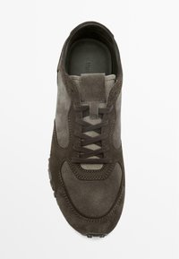 Hnědý semišový teniska s hladkou texturou, vybavená přední šněrovací částí, polstrovaným jazykem a jemnými detaily švů. Gumová podrážka.