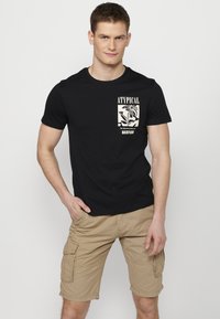 Melna kokvilnas t-kreklu ar priekšējo grafiku, kurā ir ziedu dizains un teksts. Apvienots ar bēšiem cargo šortiem, kuriem ir vairāki kabatas un brīvs piegriezums.