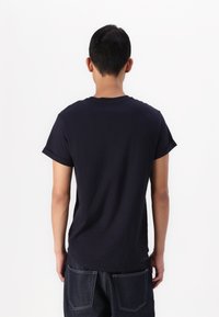 Black short-sleeve t-shirt made of cotton, featuring a crew neckline and rolled sleeves, worn with dark blue denim jeans.