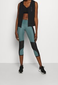 Mustat hihattomat liivit, musta urheiluliivi, turkoosit ja mustat capri-legginssit, teksturoitu kangas, kontrastivärit, ja mustat urheilukengät.