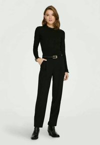 Schwarzes, tailliertes Langarmshirt mit strukturiertem Saum, kombiniert mit hochgeschnittenen schwarzen Hosen und schwarzen Stiefeletten; insgesamt elegantes Design.