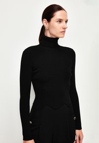 Schwarzes, geripptes Rollkragenoberteil mit langen Ärmeln und gewelltem Saum. Figurbetontes Design mit glatter Textur, kombiniert mit schwarzen Hosen mit Druckknöpfen.