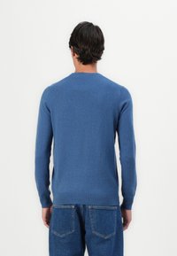Pull en tricot bleu avec des manches longues, col rond et bords côtelés. Texture lisse avec un design épuré et minimal, associé à un jean bleu clair.