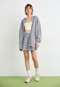 Felpa oversize grigia, crop top giallo chiaro e gonna plissettata a quadri grigia. Calzini bianchi e sneakers beige completano l'outfit.