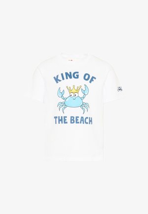 T-shirt blanc avec un crabe de dessin animé bleu portant une couronne jaune, et le texte "ROI DE LA PLAGE" en lettres bleues.