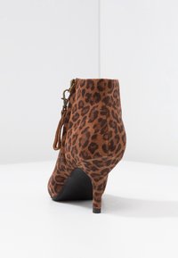 Stivale alla caviglia leopardato in suede marrone, con un tacco alto, chiusura con zip e una suola nera liscia. Decorato con un pizzo ornamentale.