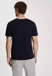 Granatowa bawełniana koszulka z klasycznym krojem, krótkimi rękawami i okrągłym dekoltem. Gładka tekstura, bez wzorów i widocznych elementów metalowych.