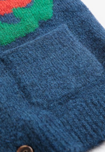 Gros plan d’un tissu tricoté bleu avec un détail de poche et une partie d’un motif multicolore en rouge et vert.