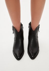 Botines negros de cuero con punta afilada, detalles sutilmente texturizados y cierres de cremallera en la parte trasera.