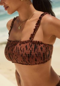 Bikini top z živalskim vzorcem v rjavi in črni barvi z nabranimi naramnicami in smockanom. Tekstura je zložena, s prilegajočim krojem.