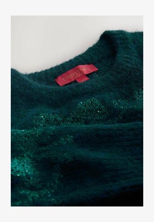 Pull en tricot vert foncé avec une finition texturée. Présente un col rond et une étiquette rouge avec l'inscription "NOËL CHEZ NEXT."