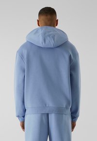 Ljusblå hoodie med en stor, justerbar huva, ribbade ärmslut och en avslappnad passform. Mjuk bomullsmaterial med en slät yta.