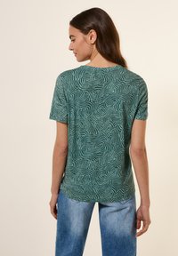 T-shirt vert �à manches courtes avec un motif ondulé blanc, col rond et ourlet arrondi. Fabriqué en tissu doux et léger.
