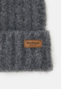 Gorro cinza de malha feito de material texturizado, apresentando uma etiqueta de couro castanho com "Barbour" e "England" em relevo. Design grosso e canelado.