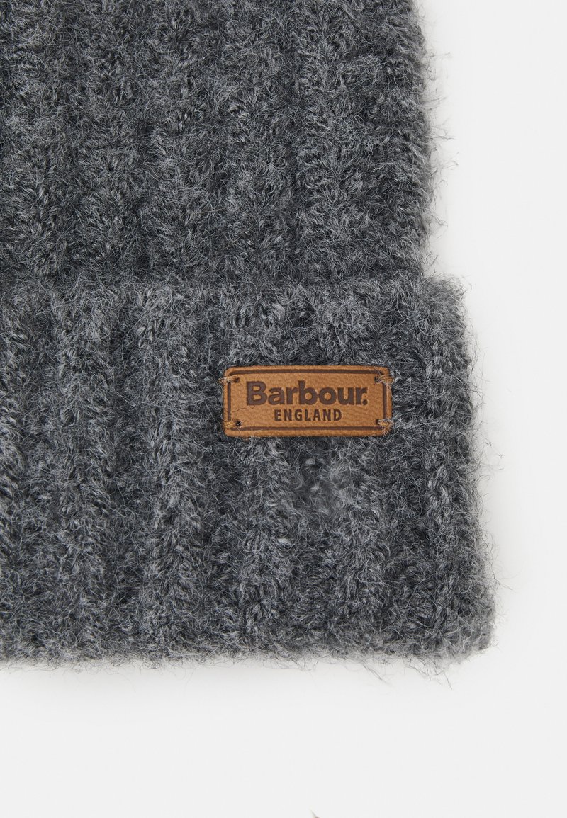 Gorro de punto gris hecho de material texturizado, con una etiqueta de cuero marrón que lleva grabado "Barbour" y "England". Diseño grueso y acanalado.
