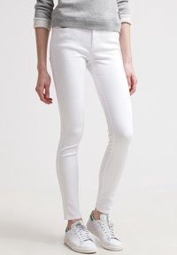 Jeans blancos ajustados con una textura suave y un diseño clásico de cinco bolsillos, combinados con una sudadera gris y zapatillas blancas.