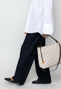 Witte blouse met lange mouwen, donkerblauwe wijde spijkerbroek, zwarte flats. Beige tas met een patroon, gouden hardware en een "P" detail.