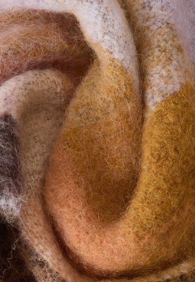 Gros plan sur un tissu doux et duveteux avec des tons terreux mélangés beige, marron et orange créant un motif texturé et roulé.