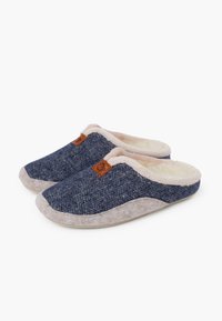 Granatowe kapcie w wzór rybiej ości z puszystym beżowym wykończeniem, miękkim teksturowanym materiałem i jasnobeżowymi gumowymi podeszwami. Zawierają małą brązową naszywkę z logo.