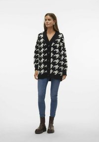 Svart och vit houndstooth-kofta med djup V-hals, knappstängning och långa ärmar, som är kombinerad med blå skinny jeans och bruna ankelstövlar.