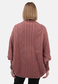 Pull en maille rose surdimensionné avec des motifs texturés en diamant et en câble, des manches côtelées et une coupe décontractée, vu de l'arrière.