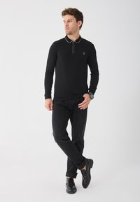 Svart långärmad polo med kontrasterande grå krage och manschetter, tillsammans med mörka jeans och svarta skor; slim fit-silhuett.