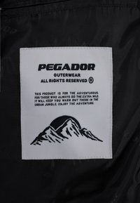 Cappotto nero con un'etichetta bianca che presenta il nome del marchio "PEGADOR" in grassetto, un grafico di montagna e le istruzioni per la cura stampate in testo nero.