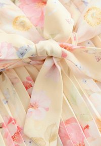 Virágmintás szövet lágy pasztell színekben, összegyűrt textúrával és megkötött masni részlettel, rózsaszín és sárga virágokkal krémszínű alapon.