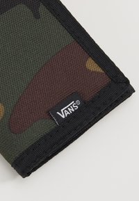 Portfel w kamuflażu wykonany z teksturowanej tkaniny, z zielonymi, brązowymi i żółtymi wzorami. Widoczne czarne przeszycia i metka z logo Vans.