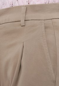 Ανοιχτό καφέ παντελόνια με λεία, υφή υφάσματος. Διαθέτει εμπρόσθιες πιέτες και επίπεδη ζώνη με θηλιές για ζώνη.