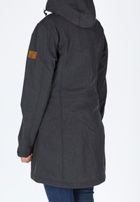 Personne vue de dos portant une veste à capuche gris foncé à manches longues et un jean bleu sur un fond uni.