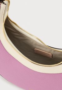 Pink and cream textured leather handbag with gold zipper partially open, showing beige fabric lining and leather brand label inside.