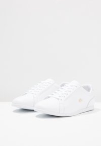 Bílé kožené tenisky s hladkou strukturou, kulatou špičkou, jemným zlatým logem a tradičním šněrováním.