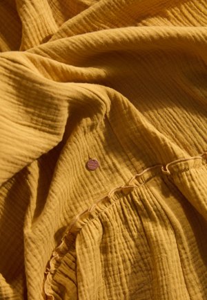 Mosterdgele textuurstof met een gekreukt effect. Bevat subtiele geraffineerde details en een klein merklabel.