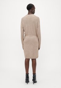 Vestito a maglia beige con maniche lunghe, vita cintata, polsini e orlo a coste, abbinato a stivali neri alla caviglia.