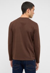 Braunes Langarmshirt mit Rundhalsausschnitt, gefertigt aus weichem Stoff. Mit einfacher Textur, geradem Saum und minimalen Nahtdetails.