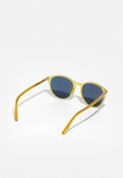 Lunettes de soleil rondes avec une monture transparente jaune et des verres bleu foncé, présentant des branches fines avec un dégradé allant du jaune à transparent.