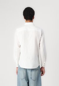 Hvid linned skjorte med lange ærmer, klassisk krave og knaplukning ved ærmerne. Skjorten har en lige pasform og et ensfarvet design. Bagfra set.