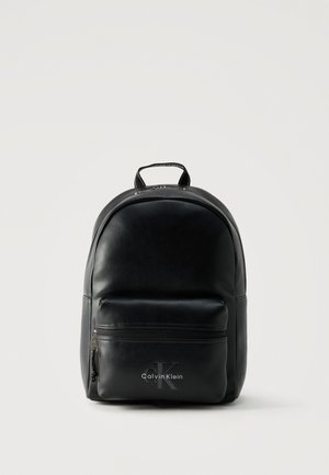 Sac à dos en cuir noir Calvin Klein avec une poche avant zippée et une poignée supérieure, présenté sur un fond clair uni.