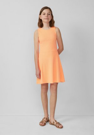 Een mouwloze, oranje jurk met een aansluitend bovenlijfje en een uitlopende rok. De stof lijkt gestructureerd. Gecombineerd met platte, bruine sandalen.