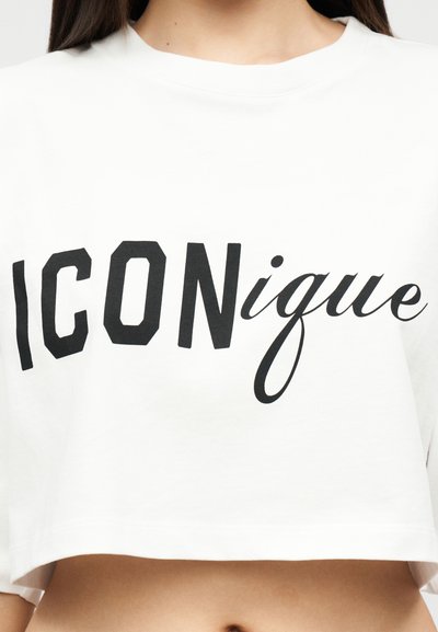 Λευκό κοντό τοπ με μαύρο κείμενο σε μικτό τύπο γραμματοσειράς που γράφει "ICONique", φορεμένο από πρόσωπο που δείχνει το στομάχι και τον λαιμό.