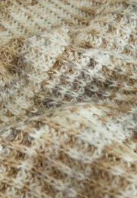 Un tissu tricoté dans des teintes crème, beige et marron clair présente un motif texturé avec des points alternés et un fil doux et duveteux.