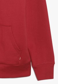Felpa rossa con tasca frontale, polsini e orlo a coste. Materiale morbido con una texture liscia e una piccola etichetta con il logo sul lato.