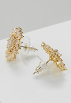 Złote kolczyki wkręty z małymi blado-różowymi kamieniami ułożonymi w wzór kwiatowy, zabezpieczone przezroczystymi plastikowymi i metalowymi zapięciami.