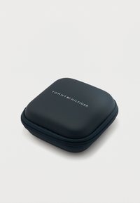 Συμπαγής μαύρη θήκη με φερμουάρ και λογότυπο Tommy Hilfiger με έμβλημα σημαίας στην κορυφή, τοποθετημένη σε απλή ανοιχτόχρωμη επιφάνεια.