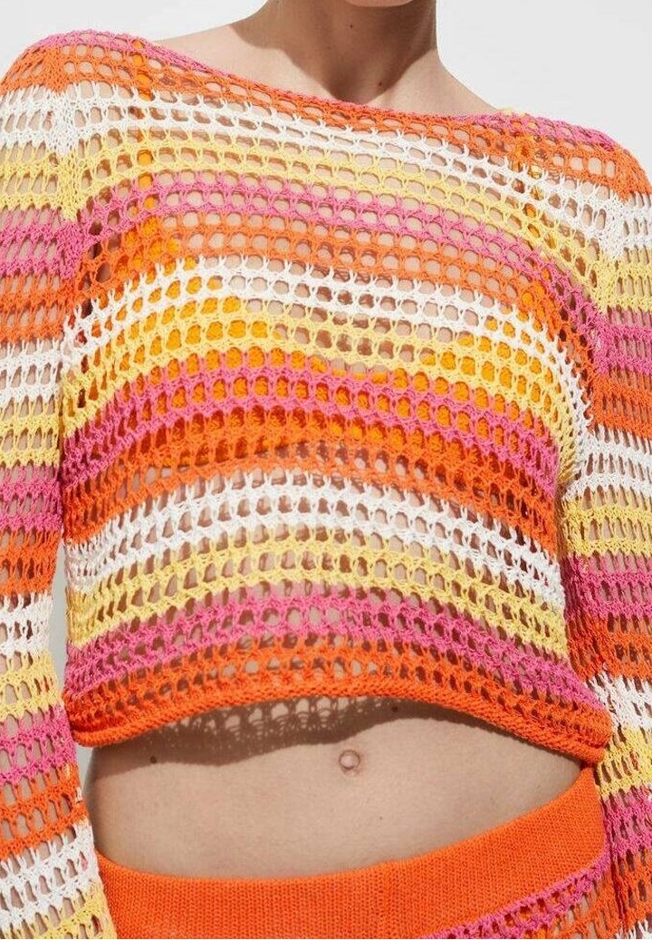 Femme portant un crop top en crochet multicolore avec des rayures orange, rose, jaune et blanc et un bas orange taille haute assorti.