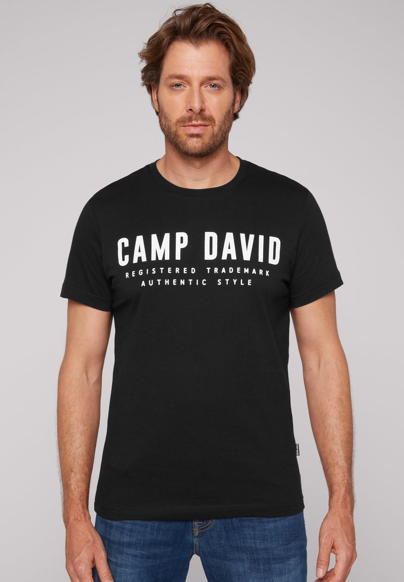 Camiseta de algodón negra con mangas cortas, con un texto blanco y audaz "CAMP DAVID" en el pecho y texto adicional abajo en fuente más pequeña.