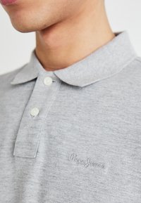 Gray polo shirt made of soft fabric, featuring a classic collar, button closure, and subtle embroidered logo on the chest.
