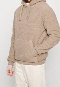 Sudadera con capucha de forro polar beige con superficie texturizada, capucha ajustable con cordón, bolsillo frontal y puños y dobladillo acanalados. Corte casual.