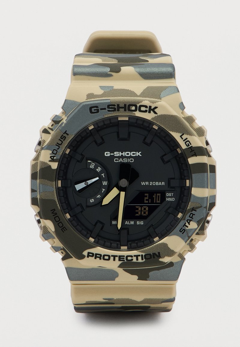 Ρολόι Casio G-Shock με αναλογική-ψηφιακή οθόνη σε καμουφλαρισμένο σχέδιο, καντράν ημέρας και κουμπιά λειτουργιών σε μπεζ φόντο.